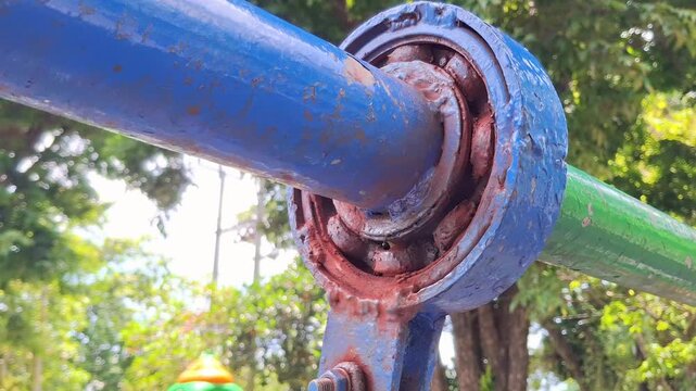 Rusty ball bearing on a blue playground swing set. Close-up of a corroded metal hinge with peeling paint. Old outdoor equipment texture for maintenance and safety concepts