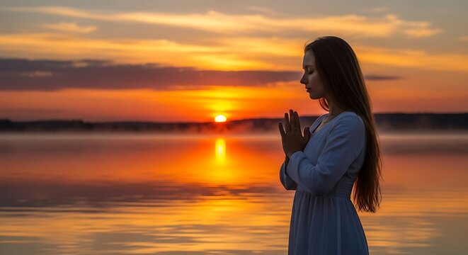 Young woman praying by the water at sunset - Powered by Adobe