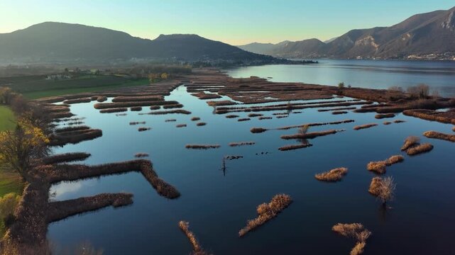 Aerial view of the tranquil waterscape along Via Sebina, reflecting the sky, and contrasting with the brown reeds along the shore, Iseo, Lombardia, Italy.