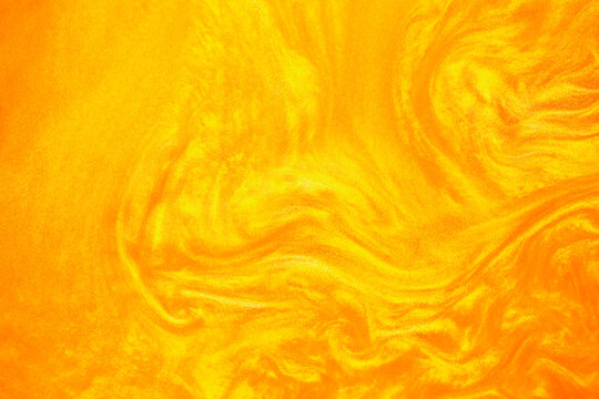 Shimmering gold abstract background. Liquid gold texture waves and swirls. Beautiful shiny yellow texture with glitter. Liquid gold metallic paint close-up.