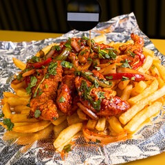 Deliciously loaded french fries topped with savory meat and fresh herbs served on foil paper