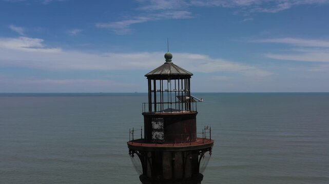 Aerial view of the majestic Morris Island Lighthouse standing tall against the vast ocean under a partly cloudy sky, Folly Beach, South Carolina, United States.