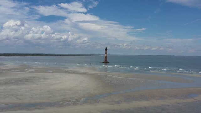 Aerial view of Morris Island Lighthouse standing tall within the ocean, a beacon surrounded by the tranquil, shimmering waters, Folly Beach, South Carolina, United States.