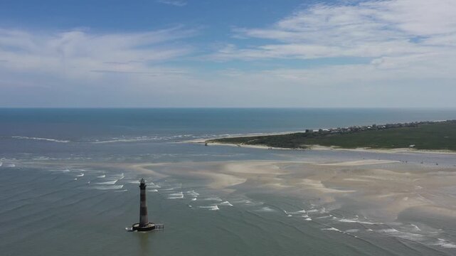 Aerial view of the Morris Island Lighthouse standing tall amidst the ocean waves and sandy shores, Folly Beach, South Carolina, United States.