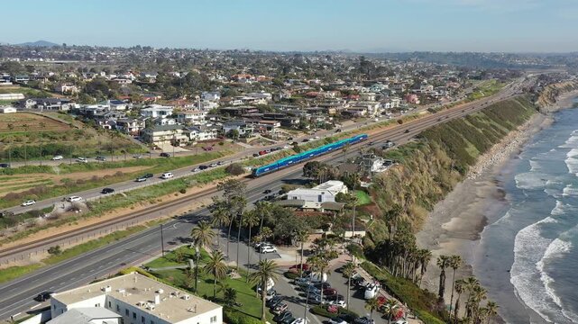 Aerial view of a blue train passing by Yogananda Ashram, contrasting with the lush fields, road traffic, and the city beyond, Encinitas, California, United States.