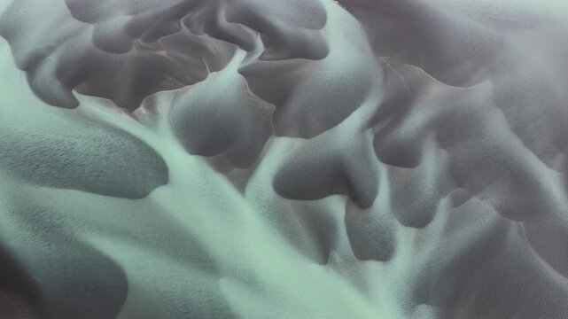 Aerial view of braided glacial river patterns creating an ethereal, otherworldly landscape of contrasting textures and tones, Iceland.