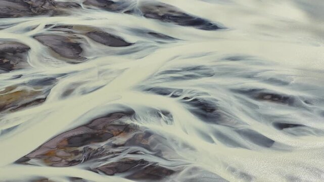 Aerial view of a braided river system with pale waters flowing between dark rocky islands, creating a mesmerizing natural pattern, Iceland.