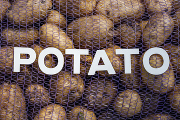 A bunch of potatoes are in a mesh bag with the word Potato written on it