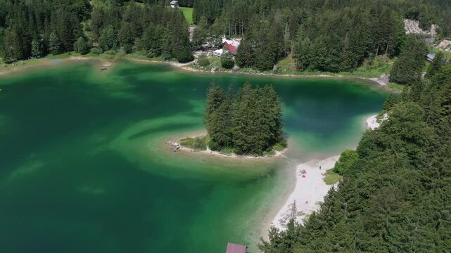 Aerial view of a serene lake with a small, tree-covered island at the center, reflecting the clear skies and lush greenery surrounding it, Udine, Friuli-Venezia Giulia, Italy.