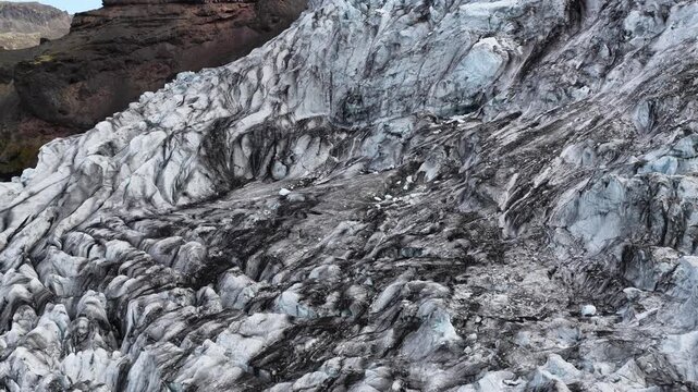 Aerial view of a glacier with contrasting black and white textures, alongside a rocky mountain, creating a stark landscape, Sveitarfelagid Hornafjordur, Iceland.