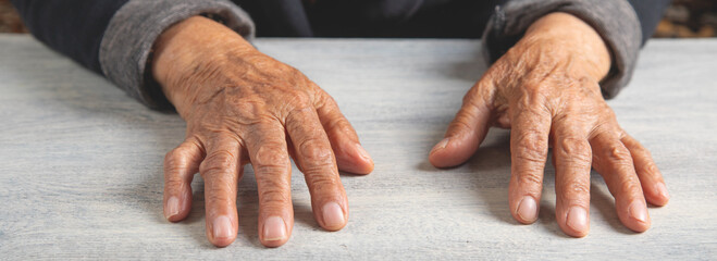 Caucasian elderly female hands on the wooden table.