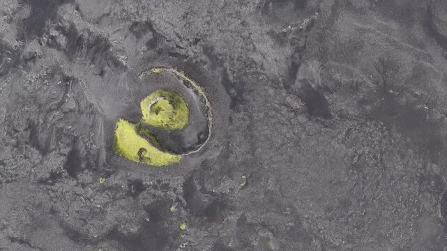 Aerial view of a vibrant green landform contrasting against the dark grey landscape, a vivid scene of nature's artistry, Skaftarhreppur, Iceland.