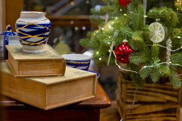 Festive scene with decorated Christmas tree, vintage books, and decorative vase, creating cozy holiday atmosphere