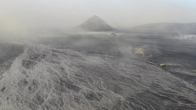 Aerial view of a stark, otherworldly landscape featuring a prominent mountain shrouded in mist with river-like patterns etched into the terrain, Skaftarhreppur, Iceland.