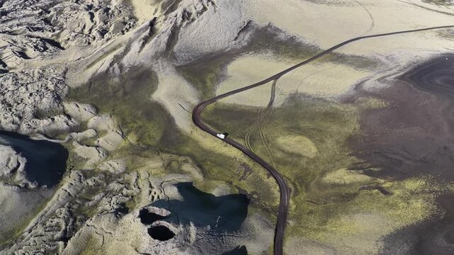 Aerial view of a lone vehicle traversing a stark, winding road through the volcanic landscape near Laki volcano, Skaftarhreppur, Iceland.
