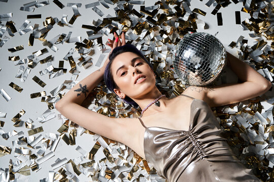 Young woman in stylish outfit poses gracefully among shiny confetti and a disco ball