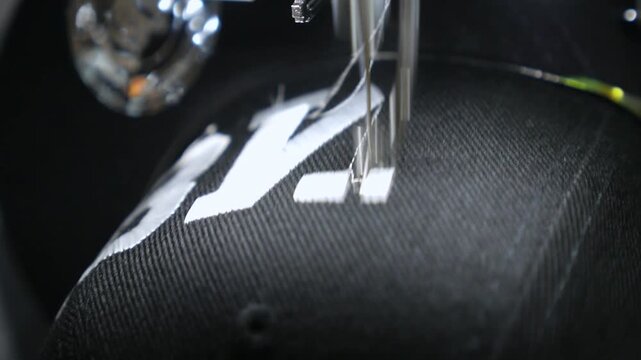 Industrial embroidery machine creating a white logo on a black baseball cap in an automated process, showcasing the precision and speed of modern textile manufacturing and customization