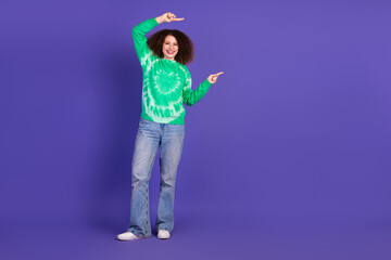 Young model in green tie dye sweater smiles and points against violet background promoting casual fashion and joyful lifestyle