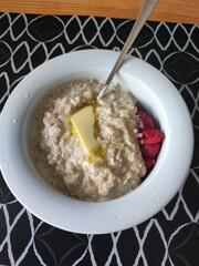 Delicious Morning Porridge. A bowl of oatmeal with raspberries and a pat of butter invites a hearty start to the day. The combination of textures and colors creates an appetizing presentation.