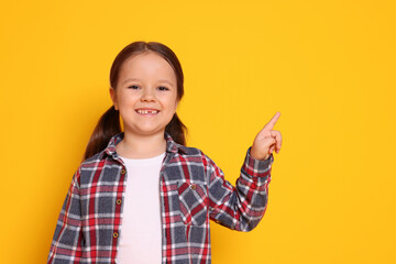 Cute little girl pointing at something on orange background, space for text