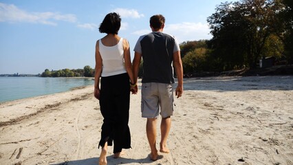 Romantic couple holding hands of each other and walking at coastline. Happy pair going along seashore at sunny day. Lovers spending time together at resort. Concept of vacation or holiday. Slow motion