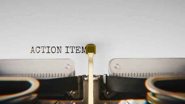 Old mechanical typewriter typing Action Items Listed in a close-up view, with metal letters striking the white paper.