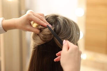 Naklejka premium Hairdresser putting clip into woman;s hair in salon, closeup
