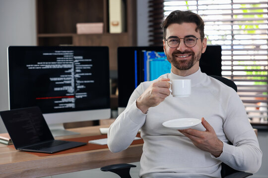 Portrait of smiling programmer in glasses with cup at workplace