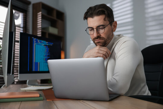 Programmer in glasses working on laptop at table in office