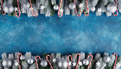 Christmas snowy fir border with silver baubles and candy canes on textured blue background