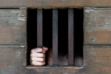 Hand gripping vertical iron bar in aged wooden wall