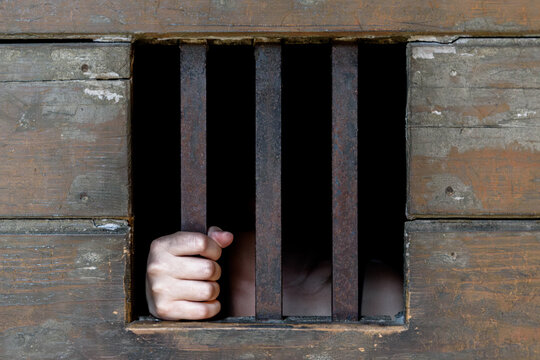 Hand gripping vertical iron bar in aged wooden wall