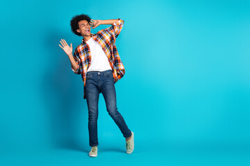 Young man wearing a colorful plaid shirt and jeans dances playfully against a bright blue studio backdrop conveying energy joy and carefree fashion
