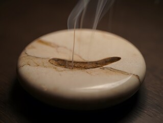Incense stick burning on a marbled stone holder with wisps of smoke