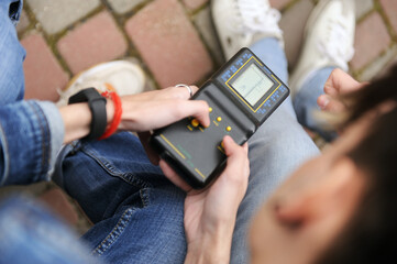 Young people engaged with a handheld device outdoors in a park setting.Technologies of the 90s.