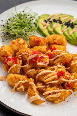 Crispy shrimp bites with spicy mayo, avocado slices and microgreens on a white plate