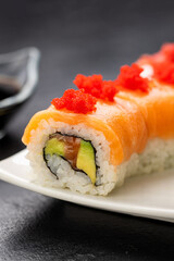 Salmon sushi roll with red roe on white plate, soy sauce, wasabi and ginger, top view