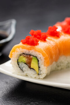 Salmon sushi roll with red roe on white plate, soy sauce, wasabi and ginger, top view