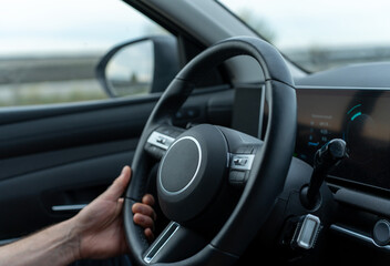 The interior of a vehicle, a man's hands holding the steering wheel of the car. Road traffic, driving a car.