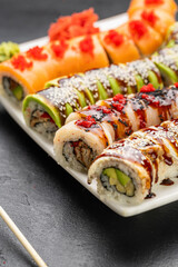 Assorted sushi rolls with salmon avocado and eel topped with sauces and sesame on plate
