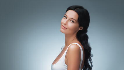Smiling Woman With Glowing Skin In White Top On Blue Studio Background