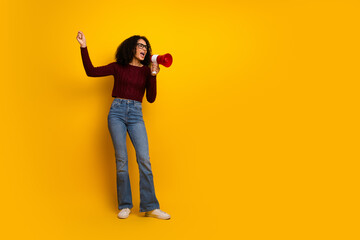Young mixed race female student with megaphone cheers against a bright yellow background showcasing casual fashion lifestyle and promotional energy