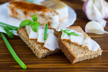 Sandwich with lard on rye bread and green onions on a wooden table
