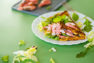 Omelette with greens and shrimps for a healthy breakfast, on a green background