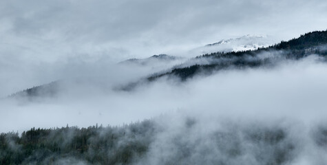 Misty Mountain Ridge Shrouded In Fog Over Forests In British Columbia, Canada During Winter