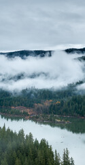 Fototapeta premium Mist Shrouded Forest and Mountain Lake in British Columbia, Canada with Foggy Peaks