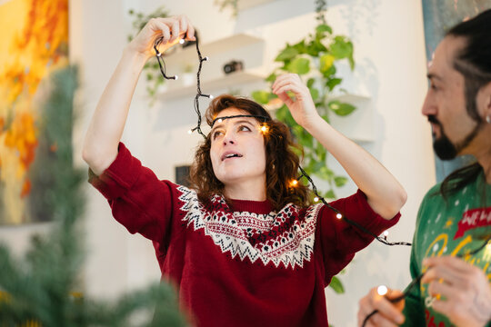 A young woman and a man decorate a home with festive string lights, creating a warm and inviting atmosphere for the holidays.