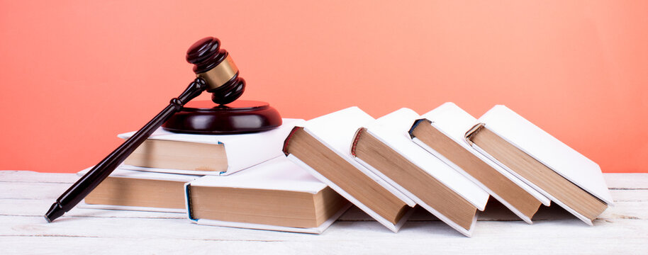 Law concept - Open law book, Judge's gavel, scales, Themis statue on table in a courtroom or law enforcement office. Wooden table, orange background.