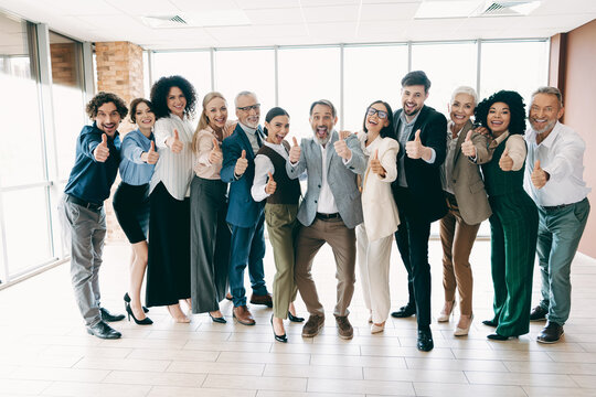 Group of professional colleagues giving a thumbs-up gesture in a modern office space promoting teamwork and collaboration - Powered by Adobe