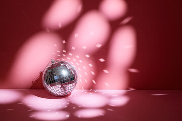 Shiny disco ball, also known as mirror ball, on a pink surface with scattered light reflections.